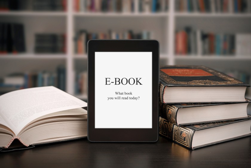 książka papierowa i e-book leżące na drewnianym stole z naturalnym oświetleniem